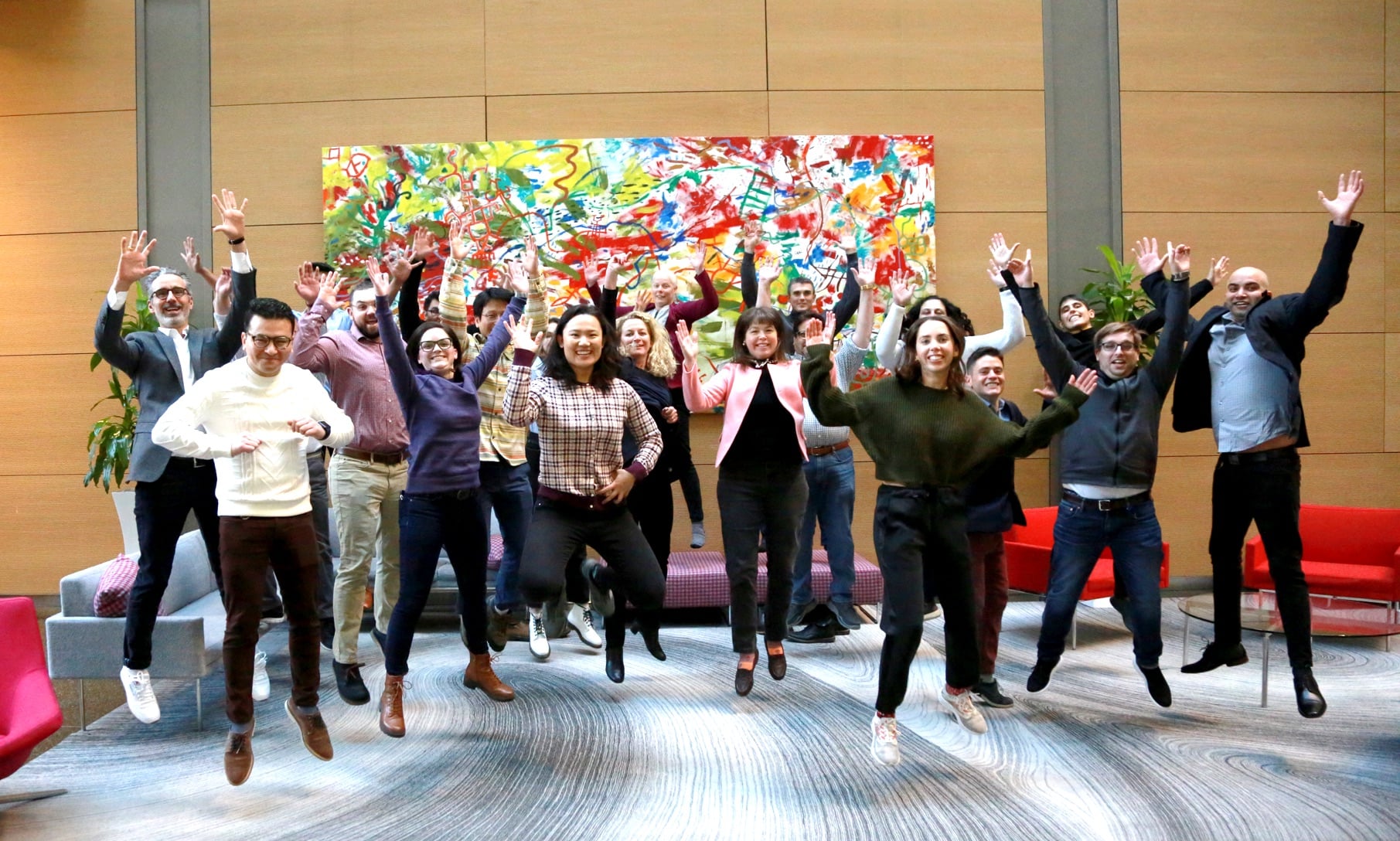 group of 10-15 people jumping and waving hands in the air in front of an abstract painting