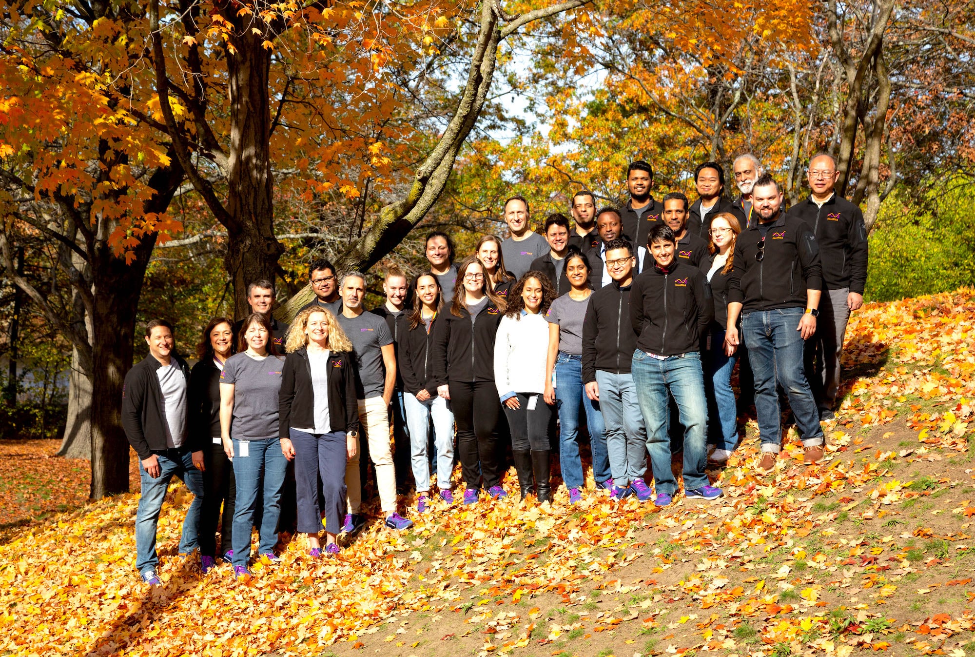 group standing & posing on a hill covered in fall leaves, with trees in the background
